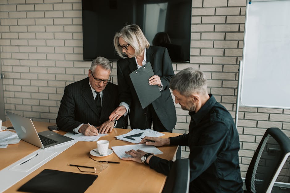 Three mature professionals in a business meeting discussing and signing documents in an office setting